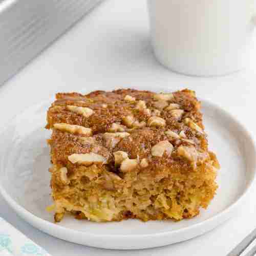 Slice of Granny Cake made with fresh milled flour on a white plate with coffee and cake pan behind
