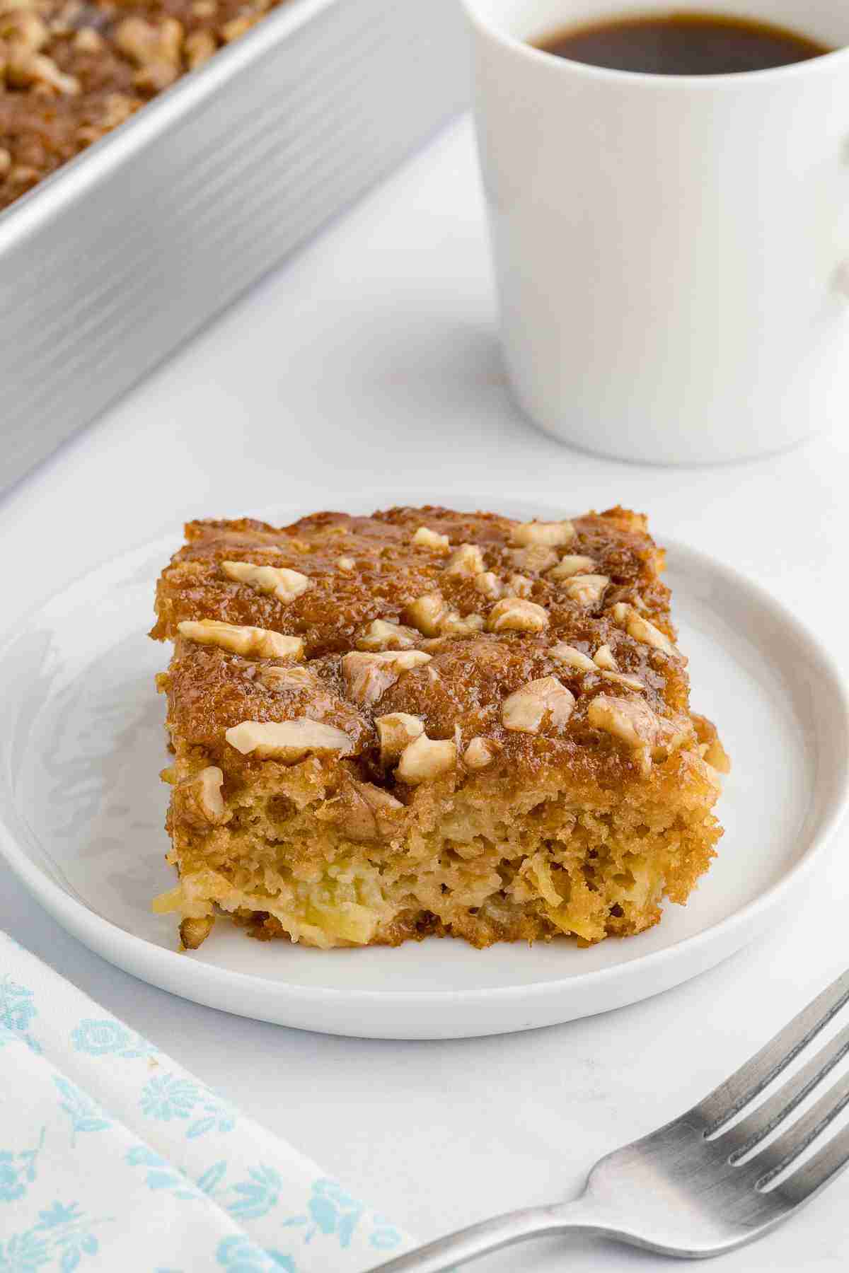 Slice of Granny Cake with fresh milled flour on a white plate with coffee and cake pan behind
