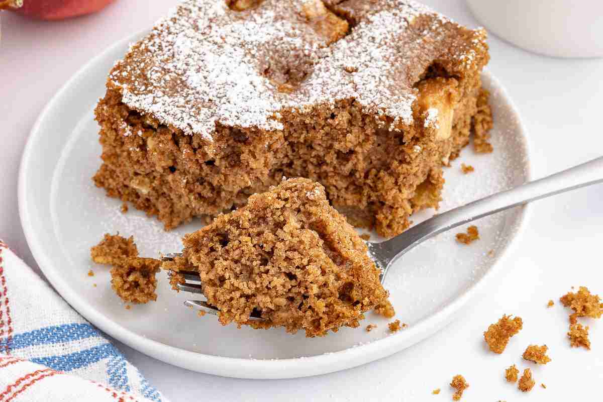 single slice of apple oatmeal cake on a white plate with bite on fork