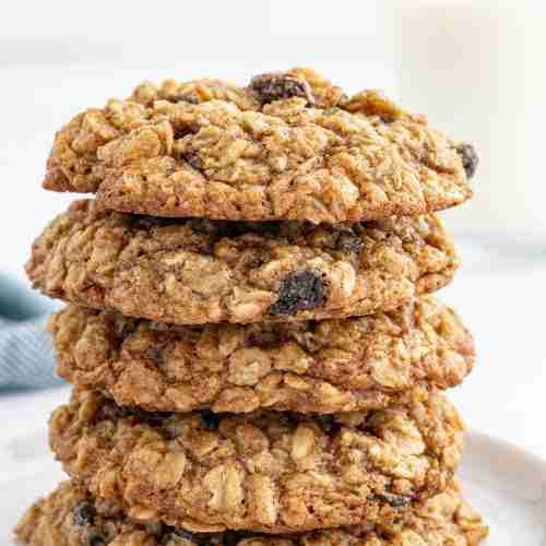 a stack of oatmeal raisin cookies with a glass of milk in the background