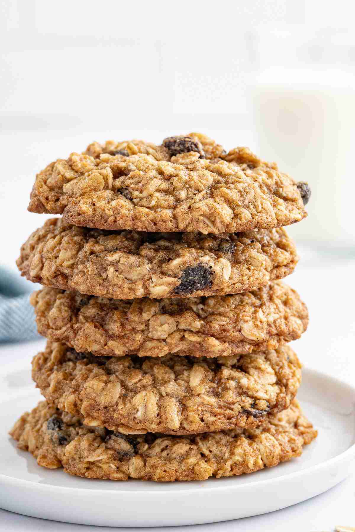 a stack of oatmeal raisin cookies with a glass of milk in the background