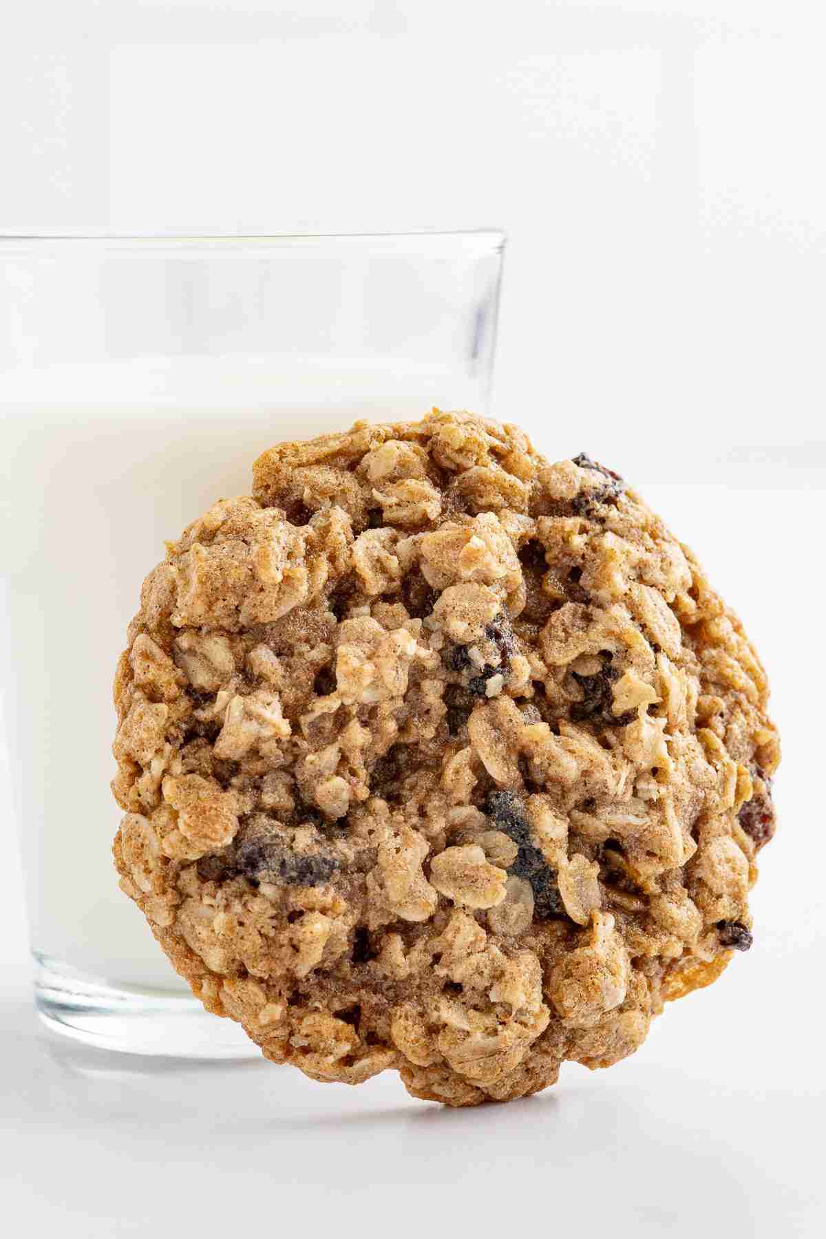 a single oatmeal raisin cookie in front of a glass of milk