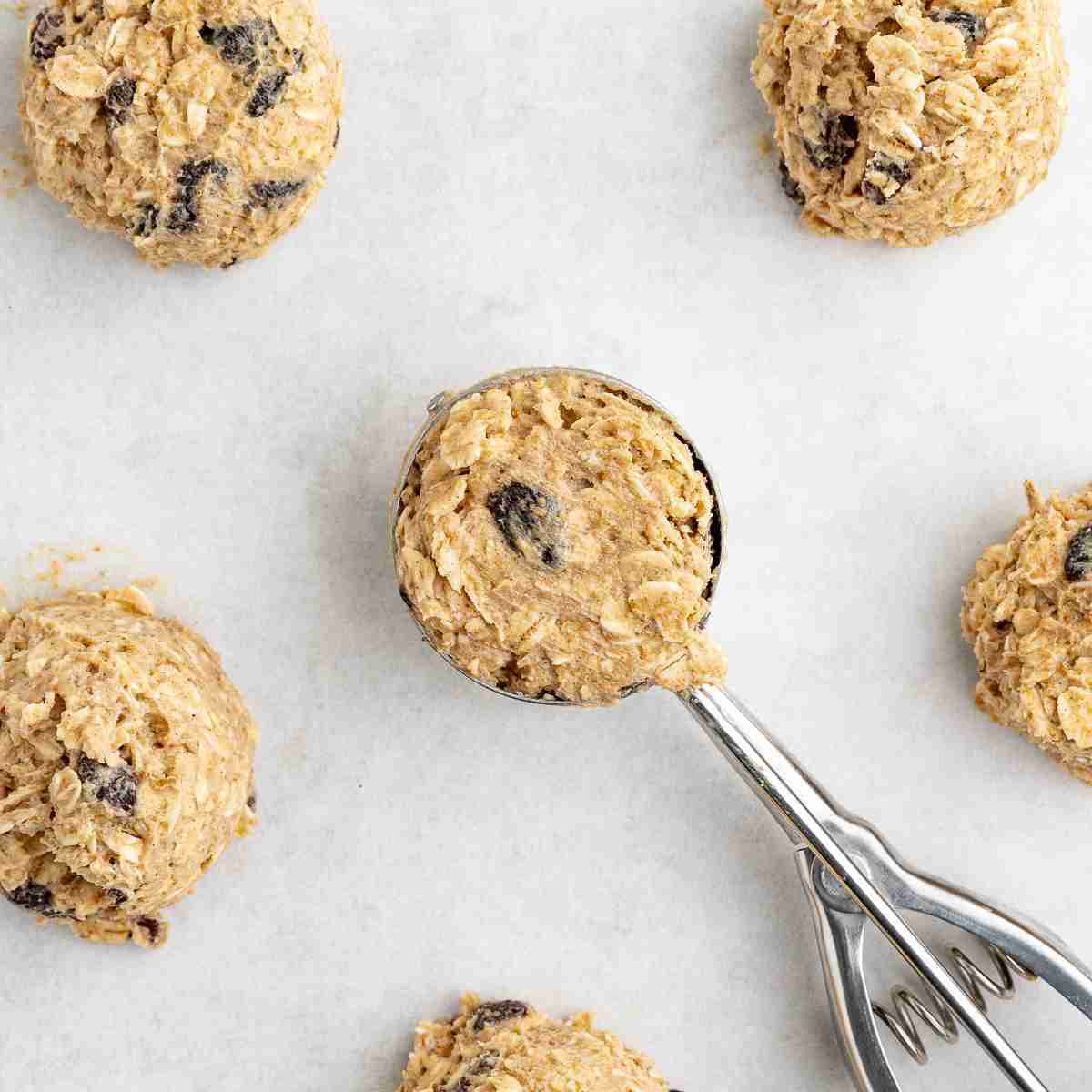 several balls of raw oatmeal raisin dough on tray with cookie scoop in the middle