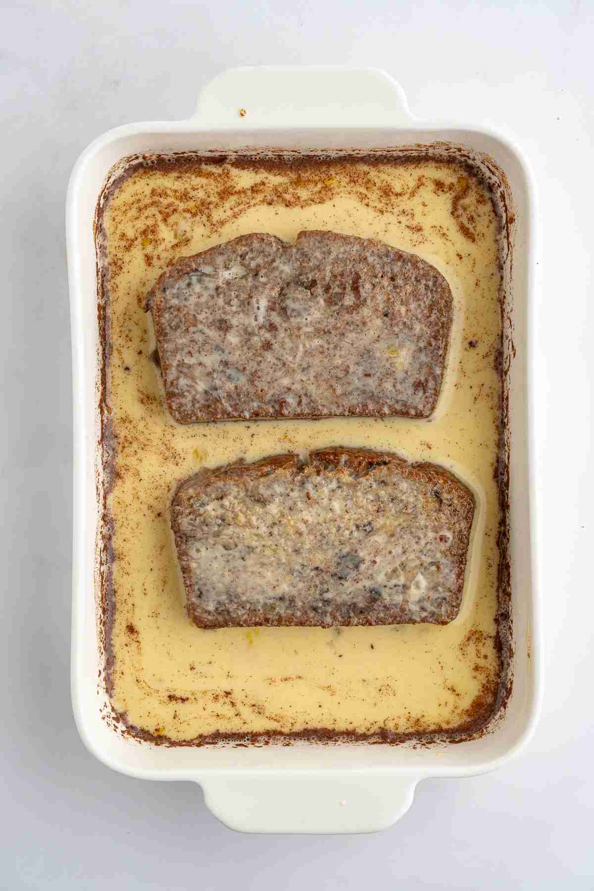casserole showing two slices of banana bread being dipped in egg mixture