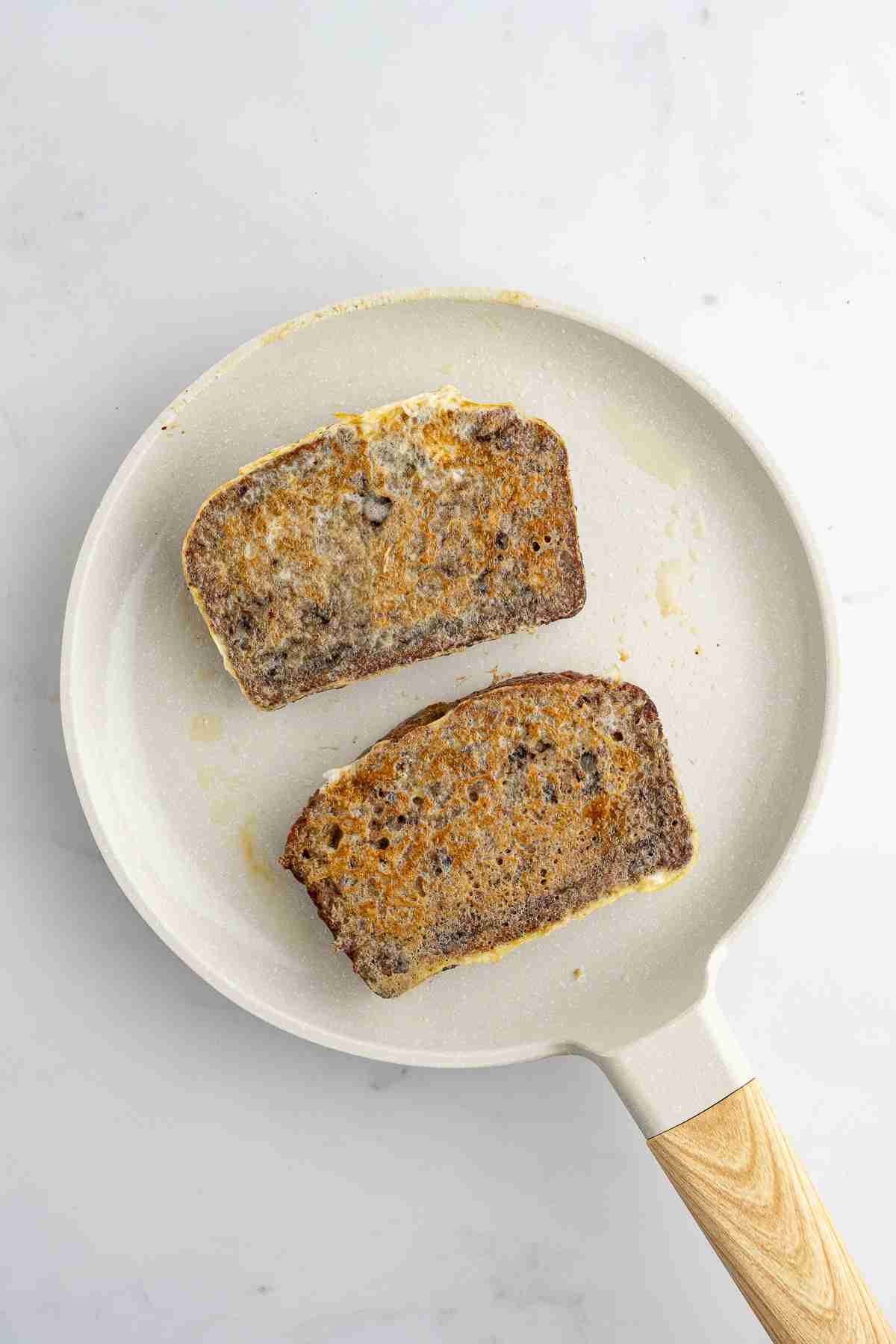 skillet showing two slices of banana bread french toast frying