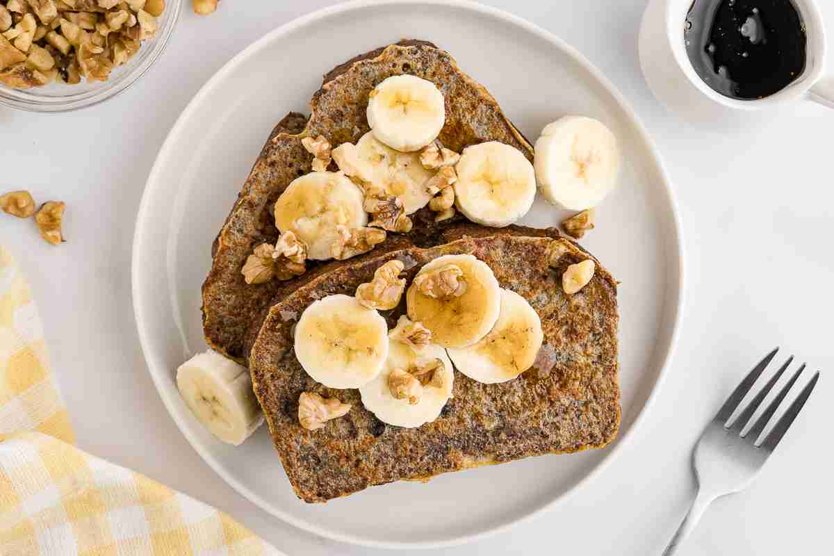 two slices of banana bread french toast with banana nuts and syrup