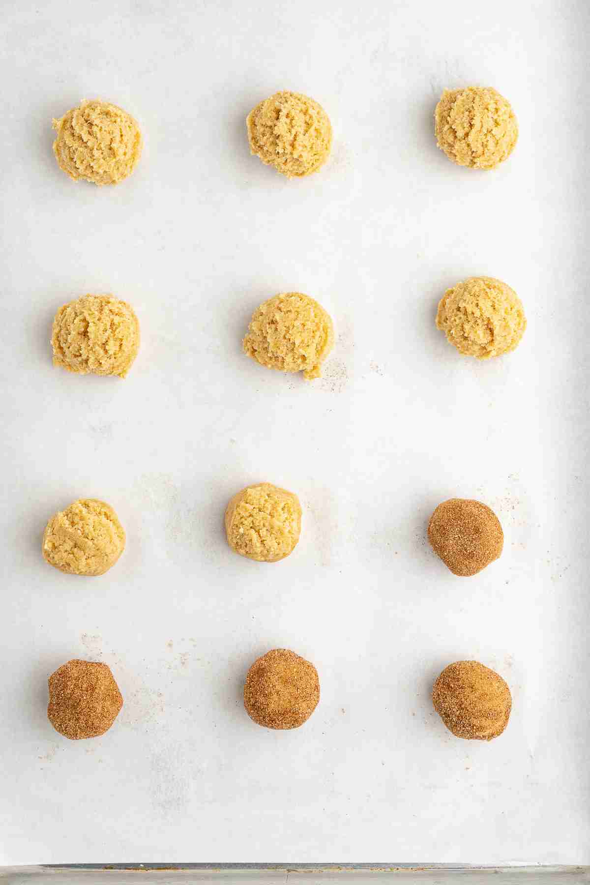 baking tray with fresh milled snickerdoodle dough balls with some of them already rolled in cinnamon sugar