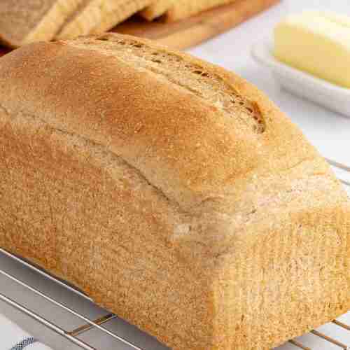 a loaf of fresh milled flour bread on cooling rack with sliced bread and butter in the background