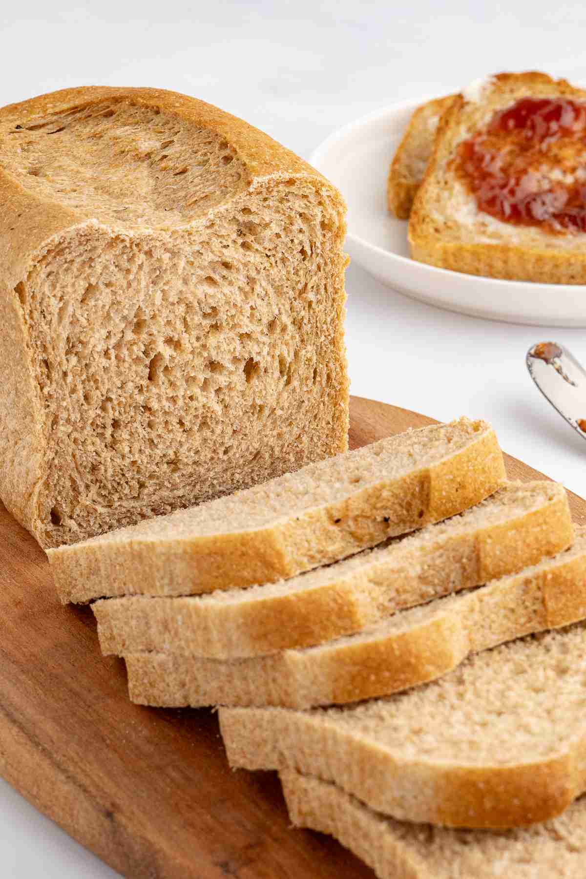 cut fresh milled flour bread loaf with slices in front and a serving of fresh milled toast with butter and jelly in the background