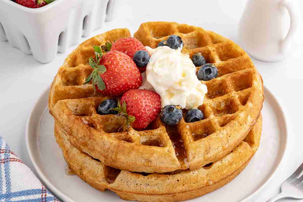 close up of fresh milled flour waffles with whipped cream and berries on white plate
