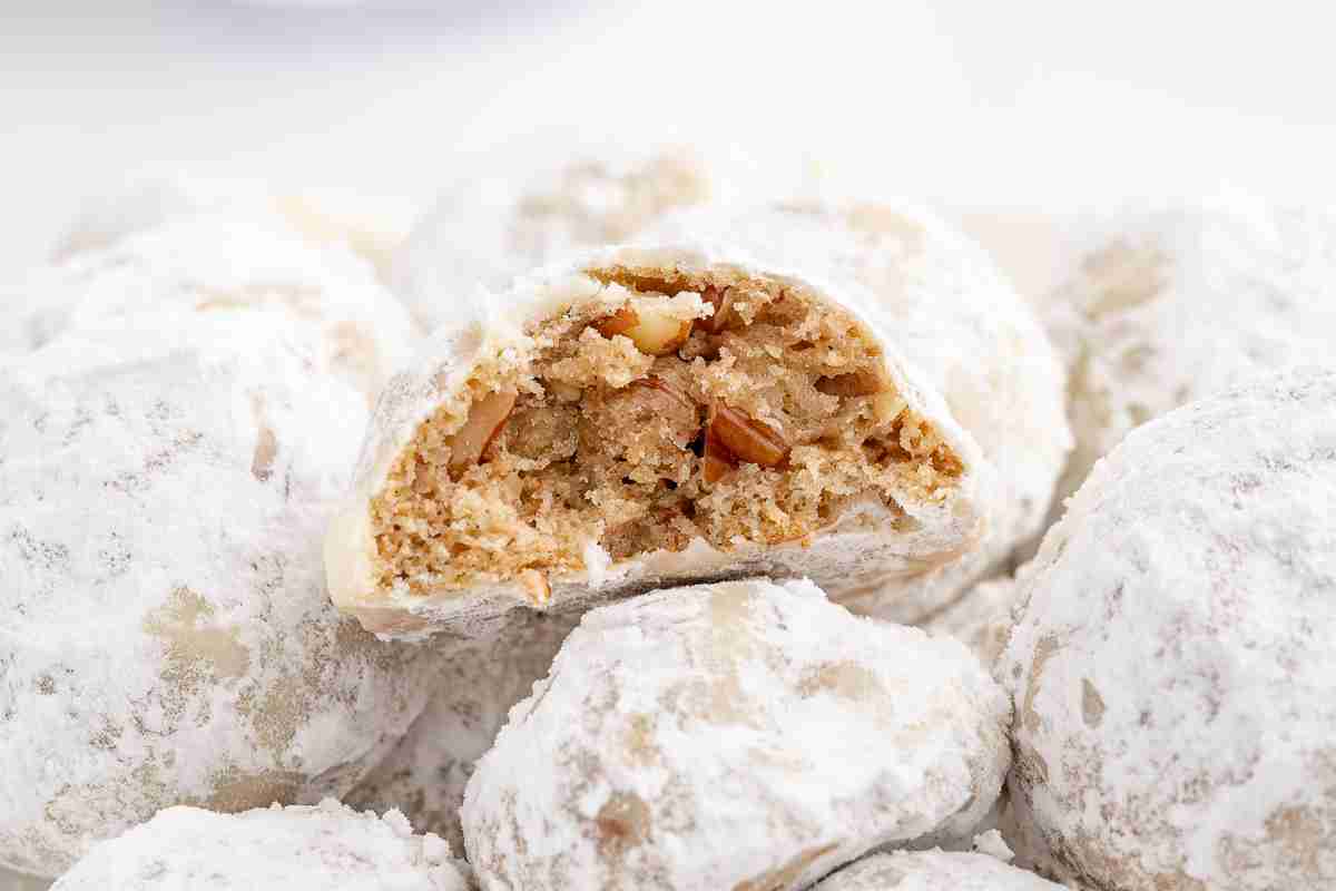 a pile of fresh milled mexican wedding cookies covered in powdered sugar with one cookie showing inside texture