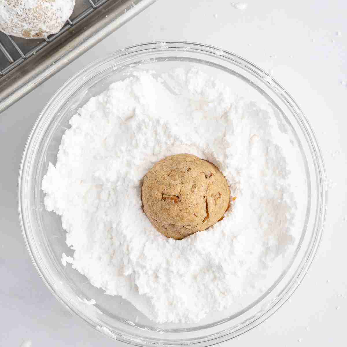rolling a fresh milled mexican wedding cookie in powdered sugar