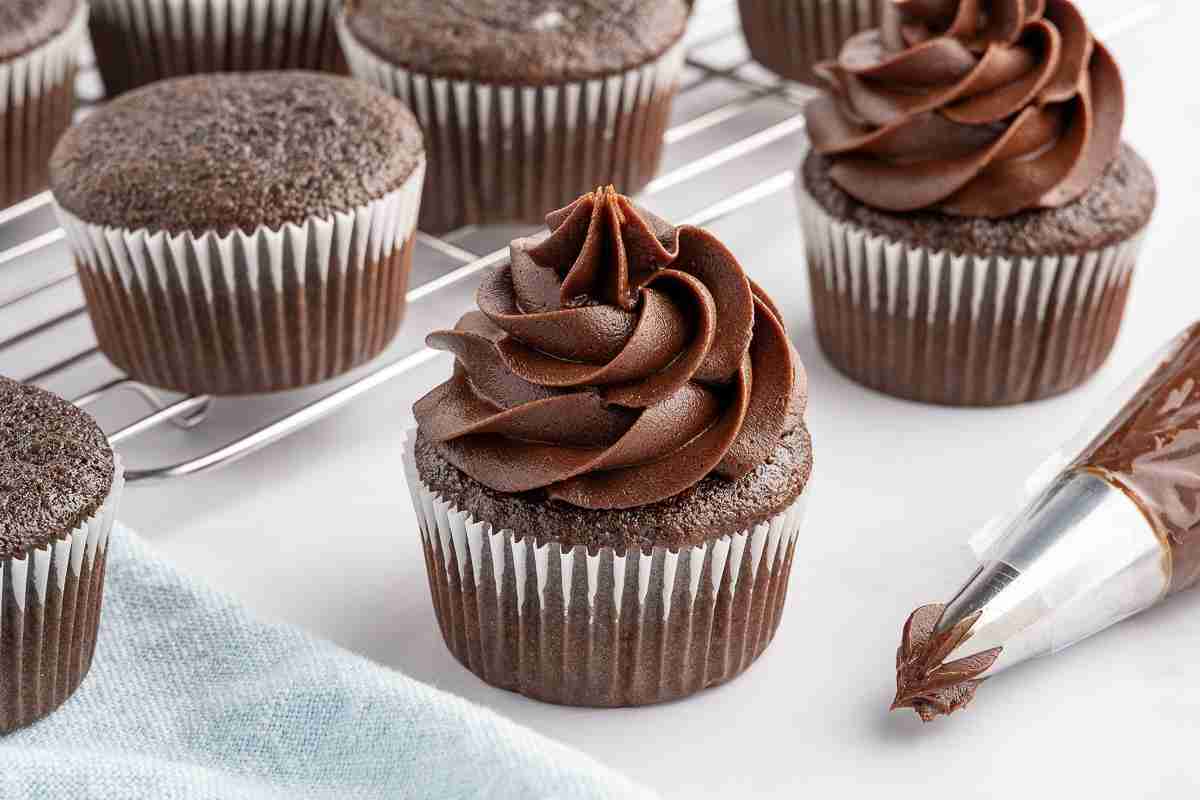 frosted fresh milled flour chocolate cupcakes on white surface with unfrosted cupcakes on cooling rack in background
