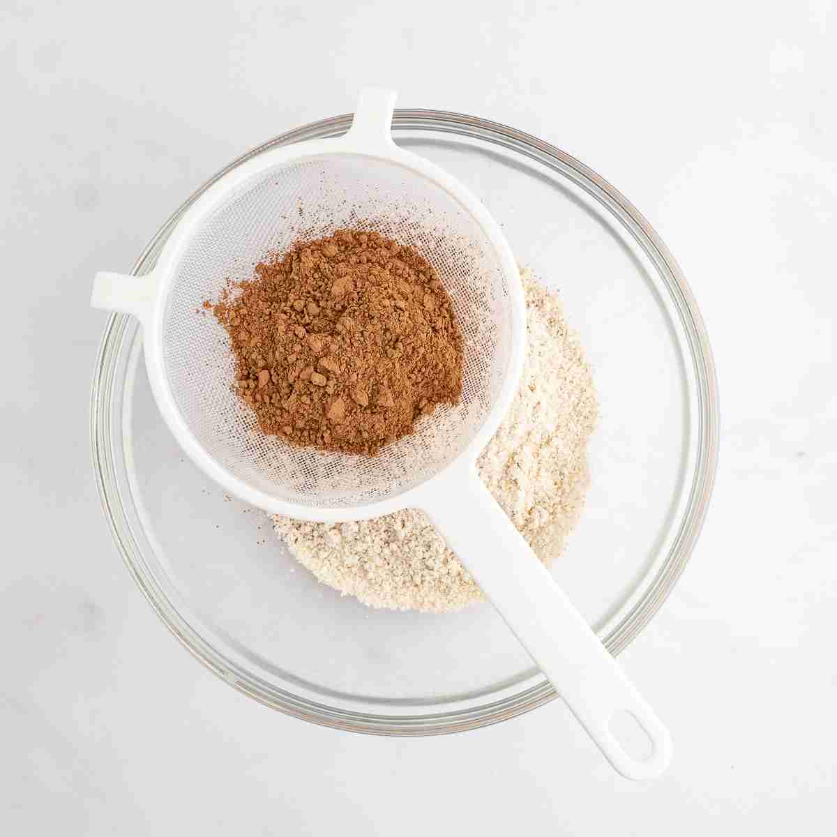mixing bowl showing cocoa being sifted over flour